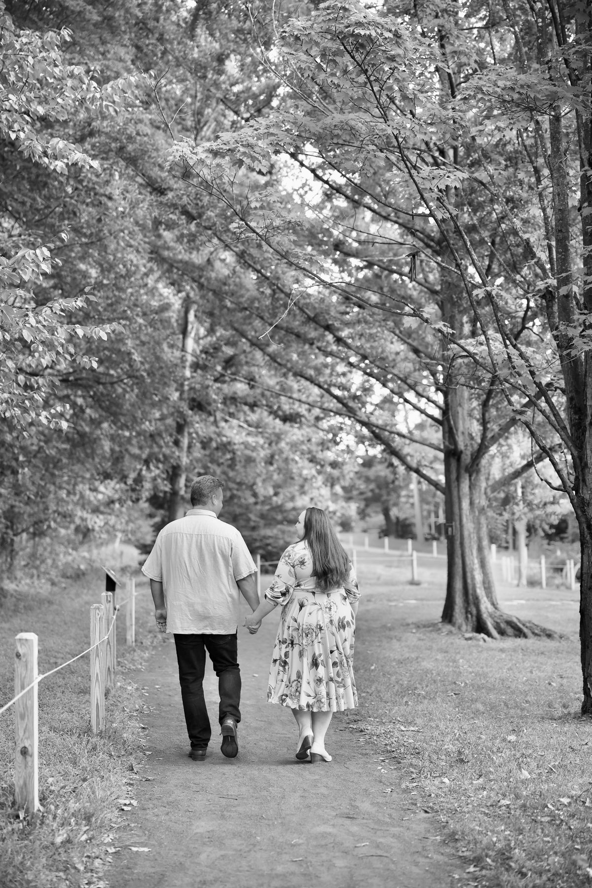 A black and white photograph of the founders of EverGrace Coffee, husband and wife, holding hands and walking away down a tree-lined path in a park.