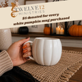 A hand holds a white ribbed pumpkin-shaped ceramic mug on a burlap placemat in a cozy fall setting. A banner at the top reads 'TWELVE12 MINISTRIES $5 donated for every white pumpkin mug purchased'.