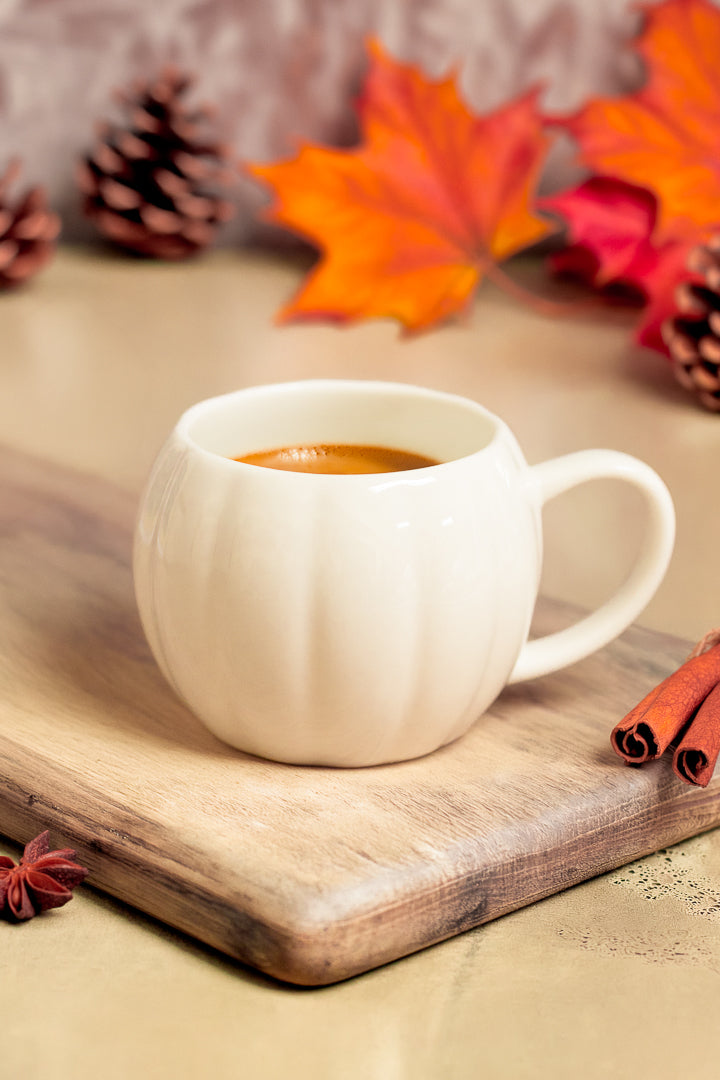 White pumpkin mug with EverGrace Coffee on a cutting board sitting on a stone counter with fall decor around it.