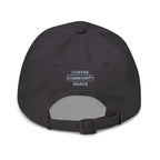 A dark charcoal gray baseball cap shown from the back, featuring the text 'COFFEE COMMUNITY GRACE' printed in white on the back panel. The cap has an adjustable dark strap with a metal buckle.