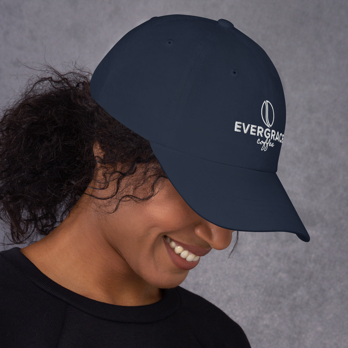 Person wearing a navy blue EverGrace Coffee cap with a logo on a gray background