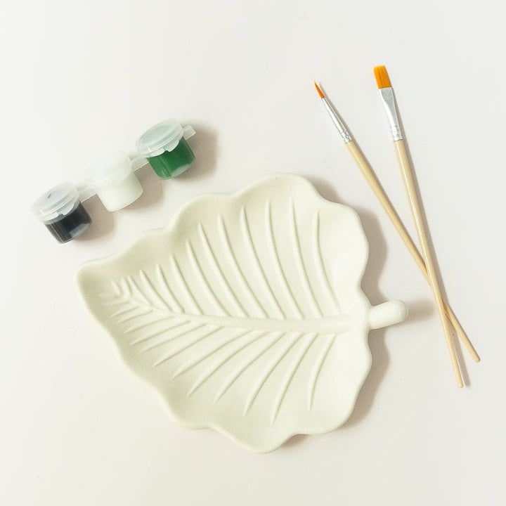 A plaster leaf-shaped paint palette with embossed leaf veins, shown on a white background with two wooden paintbrushes and small paint pots from EverGrace Coffee and Crafts