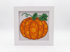A framed diamond painting or bead art piece featuring an orange pumpkin with green leaves and stem, set in a white square frame against a clean white background.